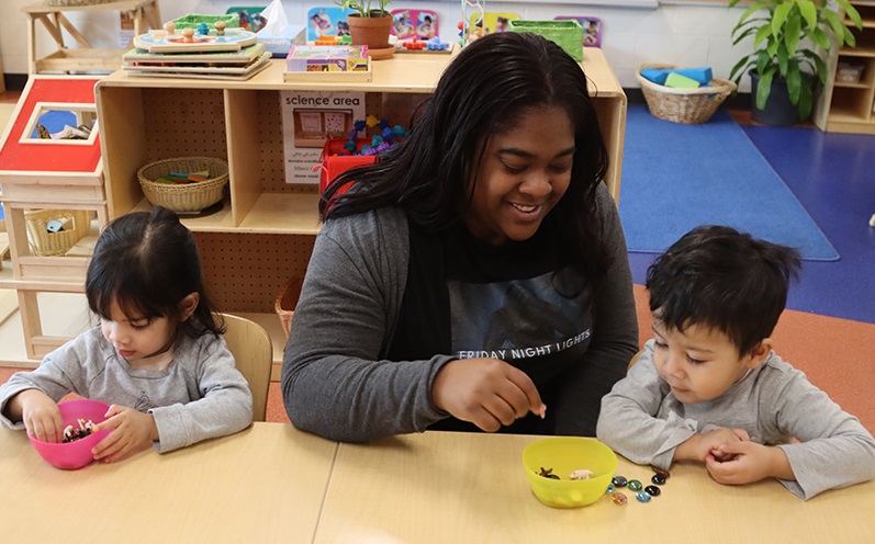 A PLASP educator sits in between two young children to encourage play with spare parts in an Early Learning and Child Care Centre